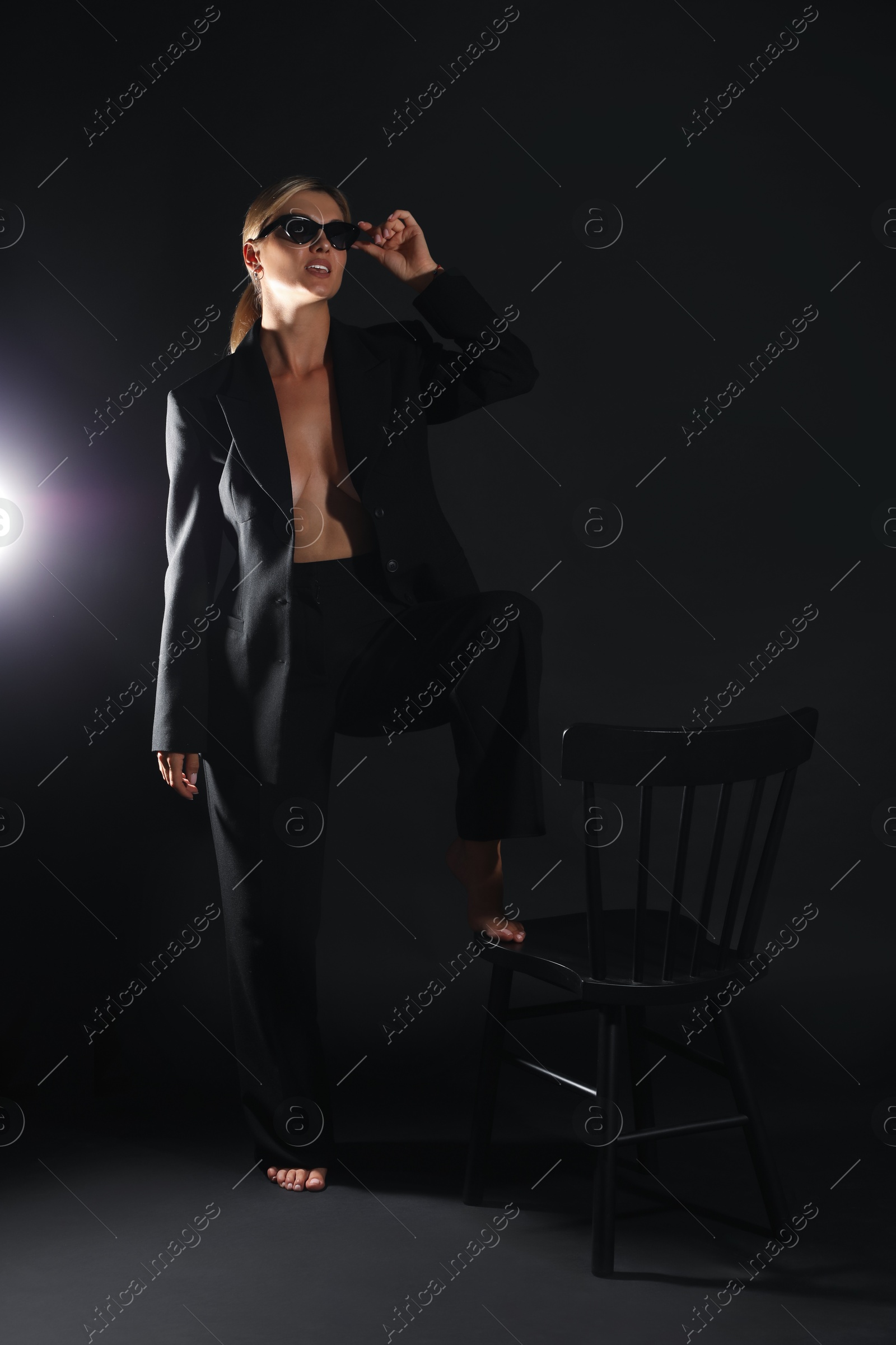 Photo of Beautiful woman in stylish suit near chair on black background