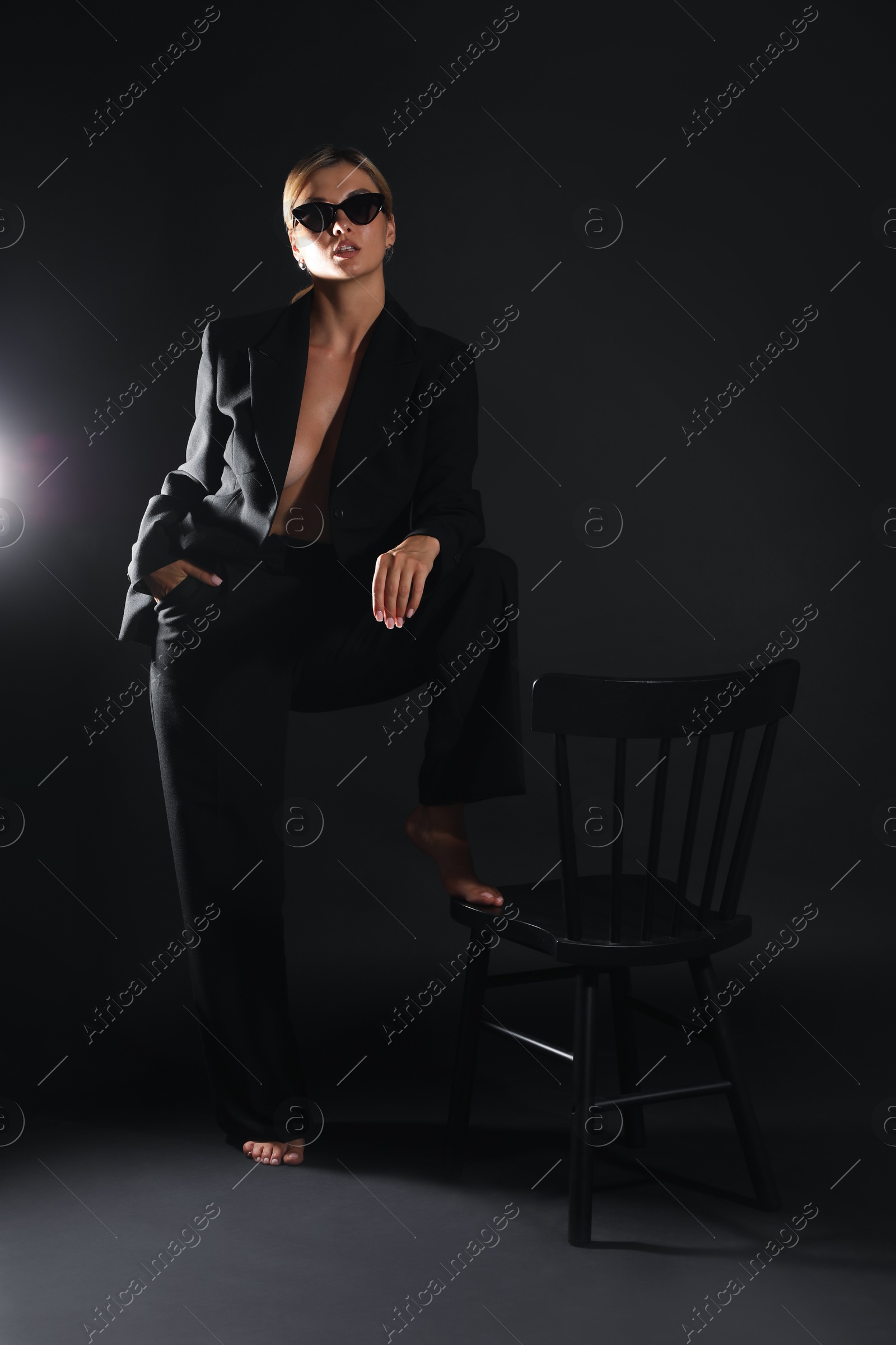 Photo of Beautiful woman in stylish suit near chair on black background