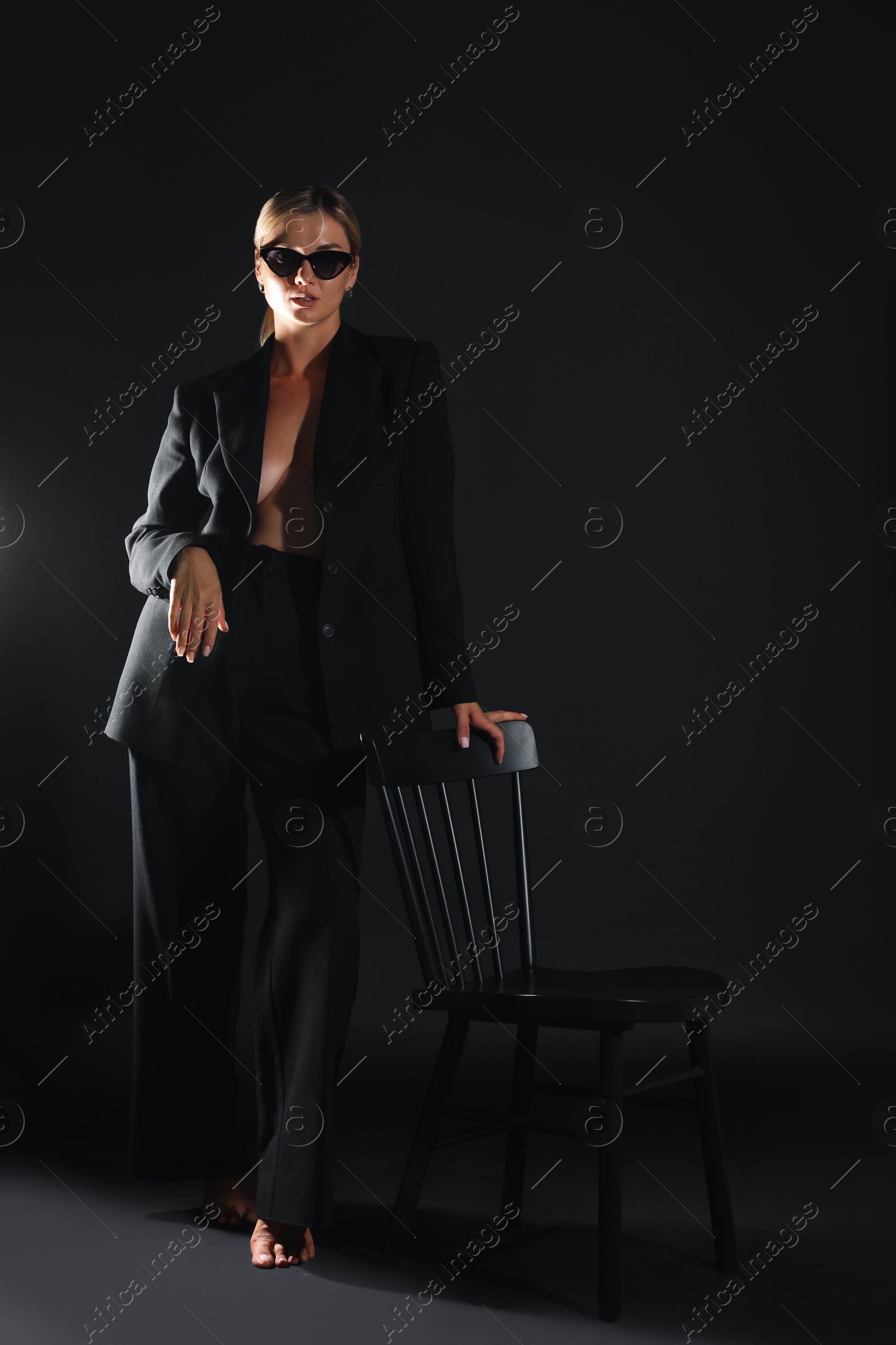 Photo of Beautiful woman in stylish suit near chair on black background