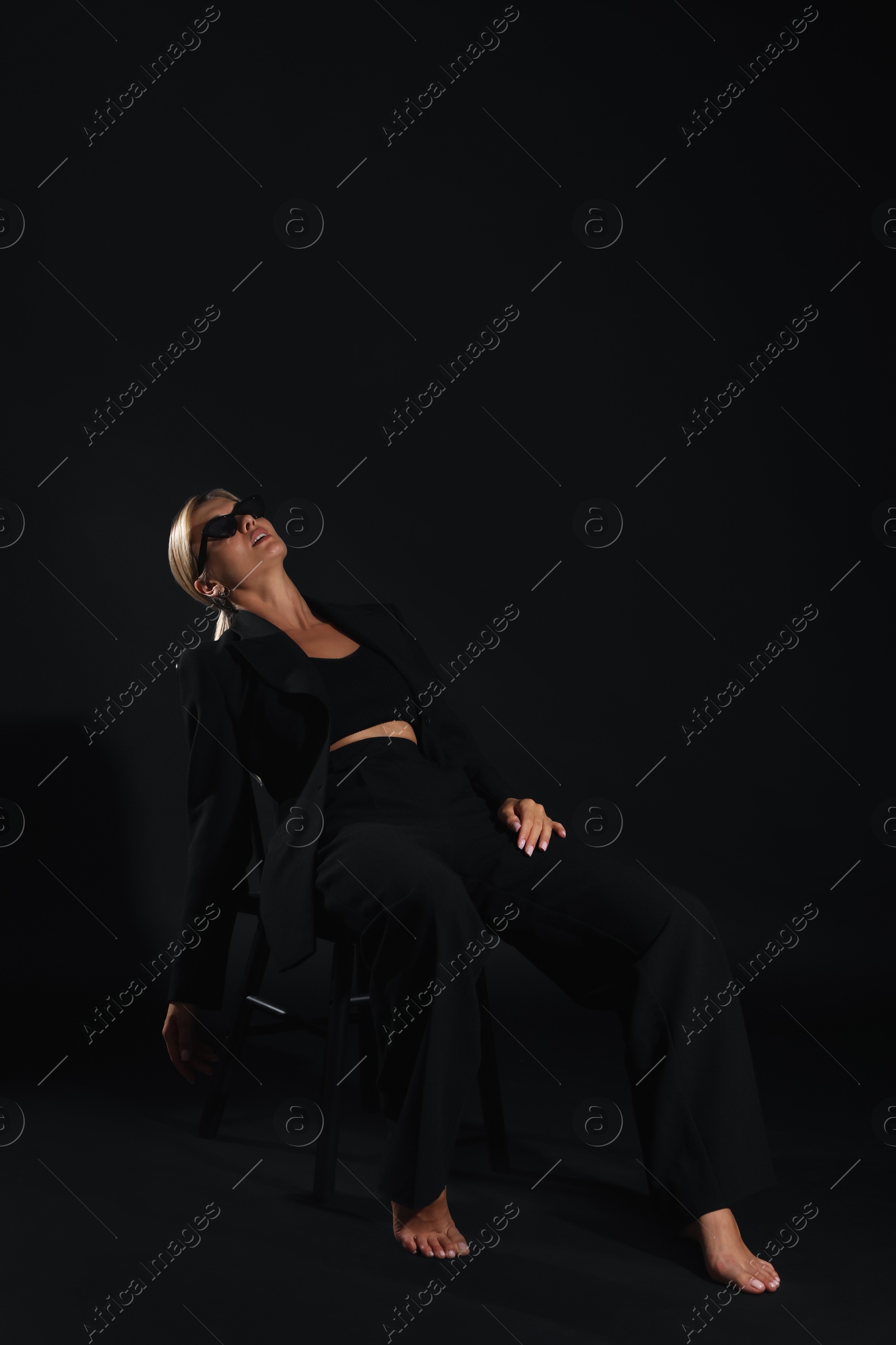 Photo of Beautiful woman in stylish suit sitting on chair against black background