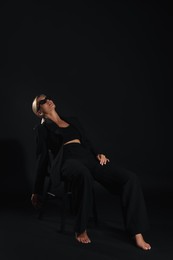 Photo of Beautiful woman in stylish suit sitting on chair against black background