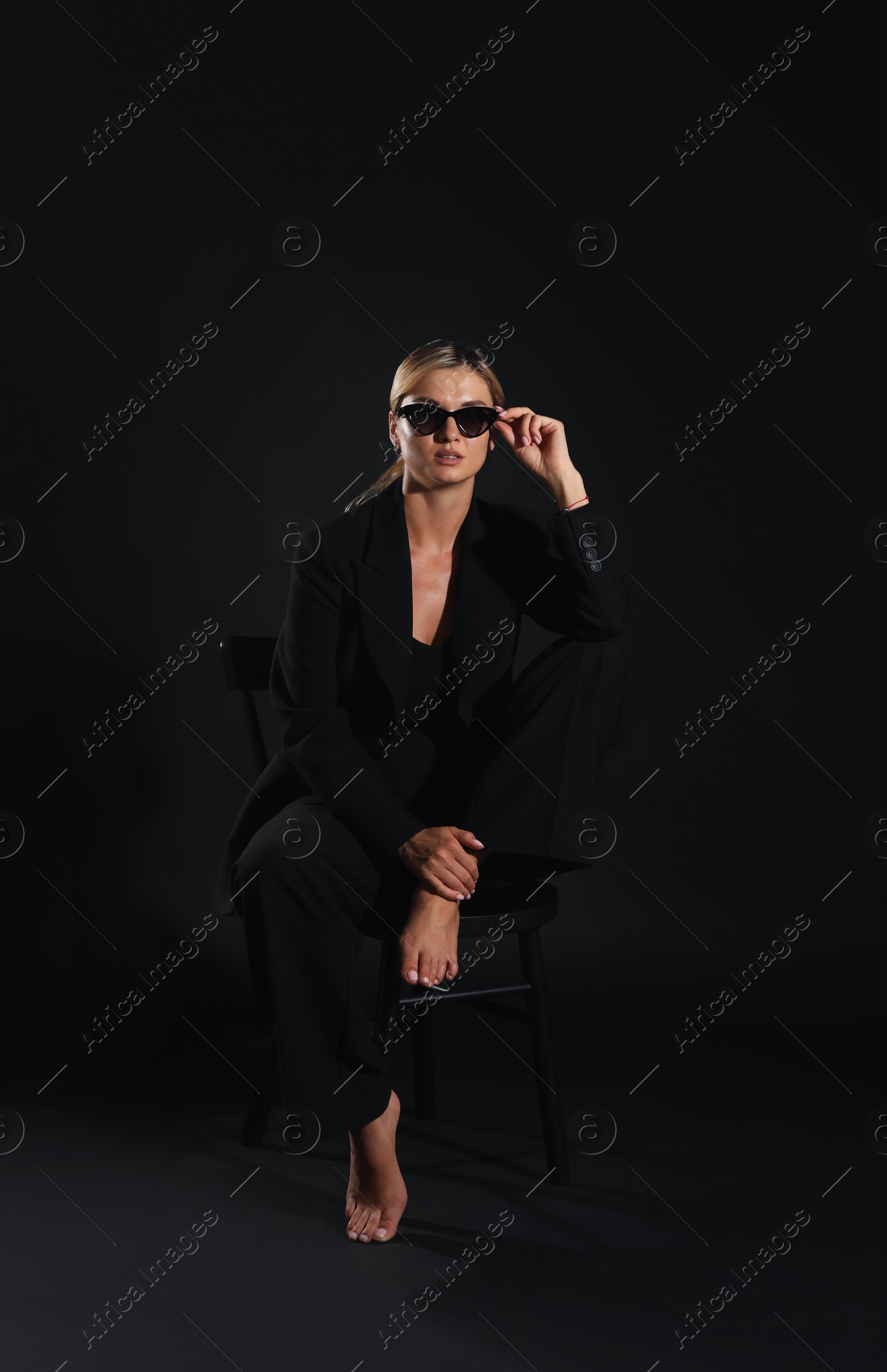 Photo of Beautiful woman in stylish suit sitting on chair against black background