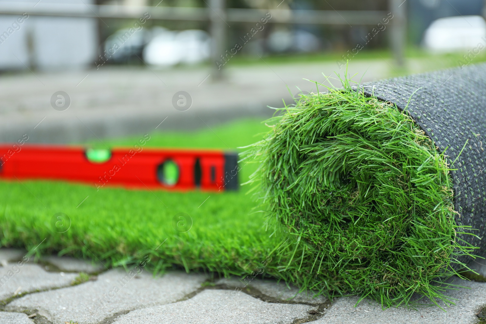 Photo of Level tool and roll of artificial turf outdoors, closeup