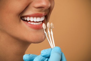 Doctor checking young woman's teeth color on beige background, closeup. Dental veneers