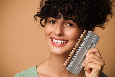 Happy young woman with teeth color samples on beige background. Dental veneers