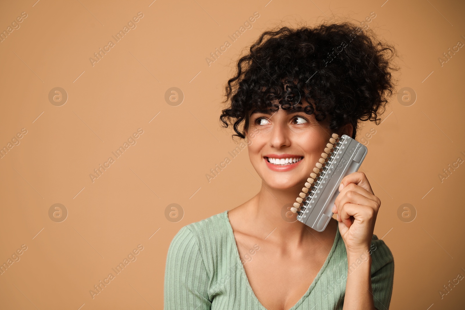 Photo of Happy young woman with teeth color samples on beige background, space for text. Dental veneers