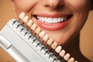 Smiling woman with teeth color samples on beige background, closeup. Dental veneers