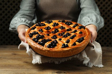 Photo of Woman holding tasty homemade pie with blueberries over wooden table, closeup