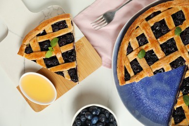 Tasty homemade pie with blueberries, honey and fork on white table, flat lay