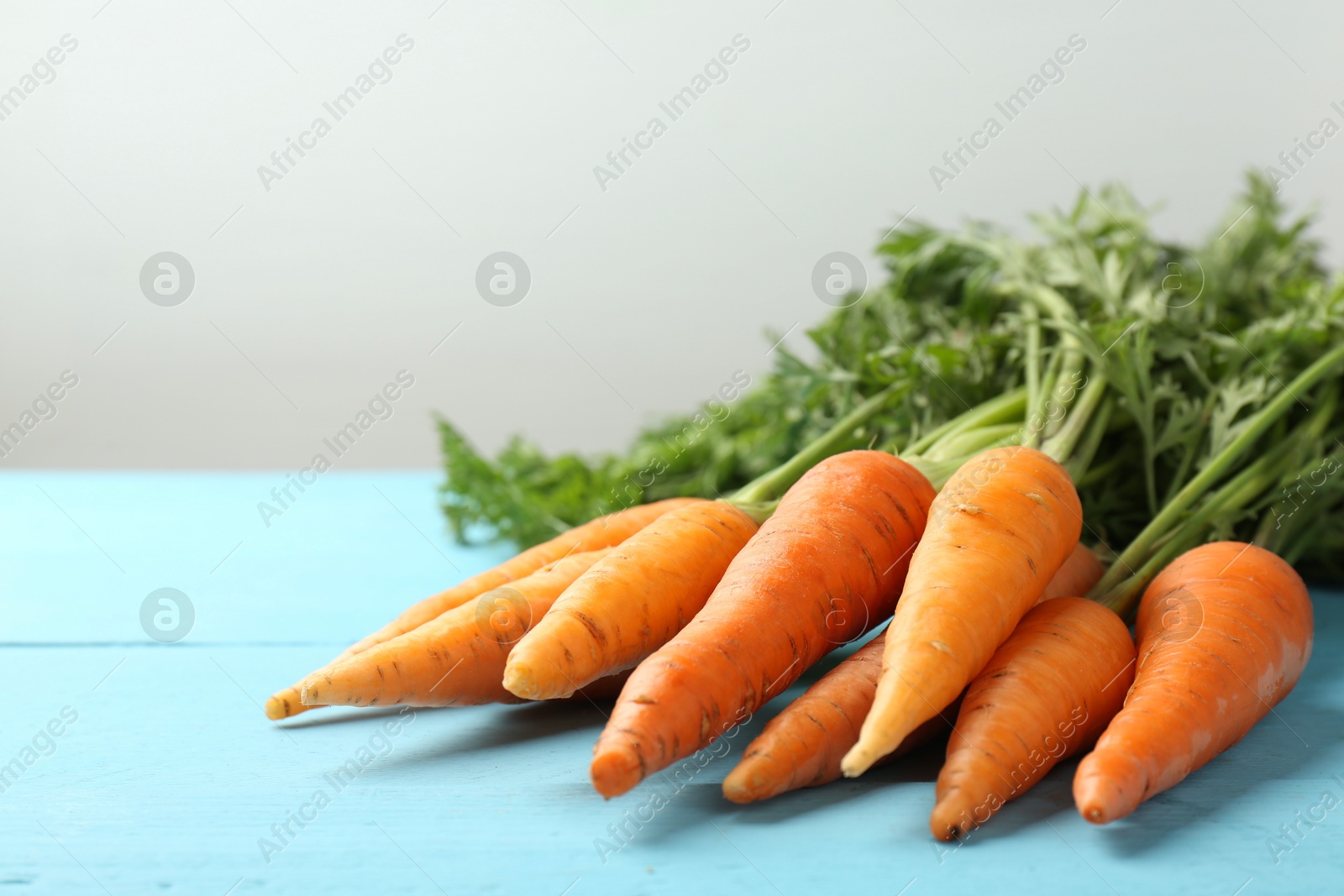 Photo of Tasty ripe juicy carrots on light blue wooden table, closeup