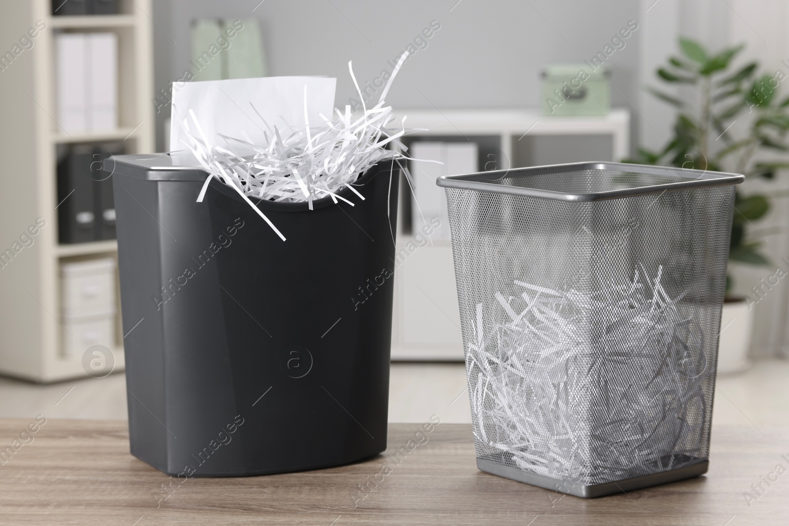 Photo of Destroying sheets with shredder and paper strips in metal bin on wooden table in office