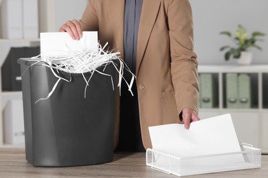 Photo of Woman destroying paper with shredder at wooden table in office, closeup