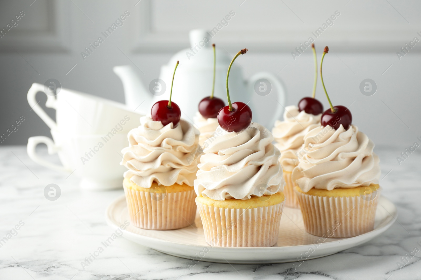 Photo of Delicious cupcakes with cream and cherries on white marble table