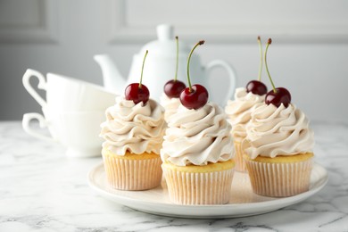 Delicious cupcakes with cream and cherries on white marble table