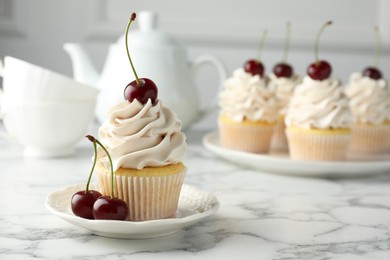 Photo of Delicious cupcakes with cream and cherries on white marble table