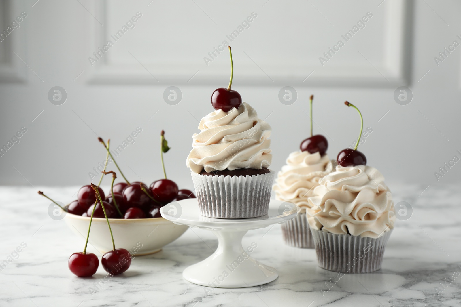 Photo of Delicious cupcakes with cream and cherries on white marble table