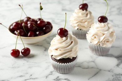 Delicious cupcakes with cream and cherries on white marble table