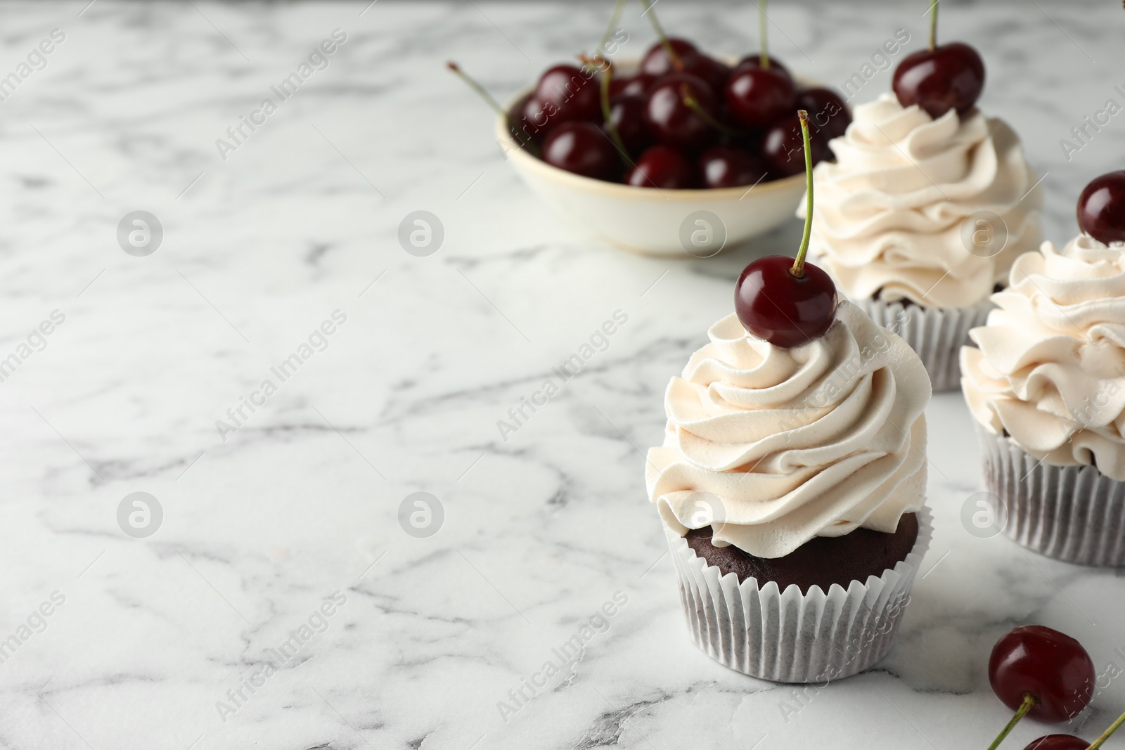 Photo of Delicious cupcakes with cream and cherries on white marble table, space for text