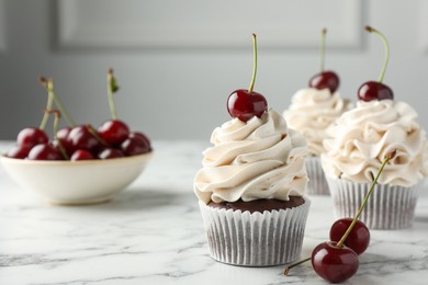 Delicious cupcakes with cream and cherries on white marble table