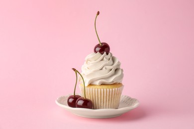 Photo of Delicious cupcake with cream and cherries on pink background