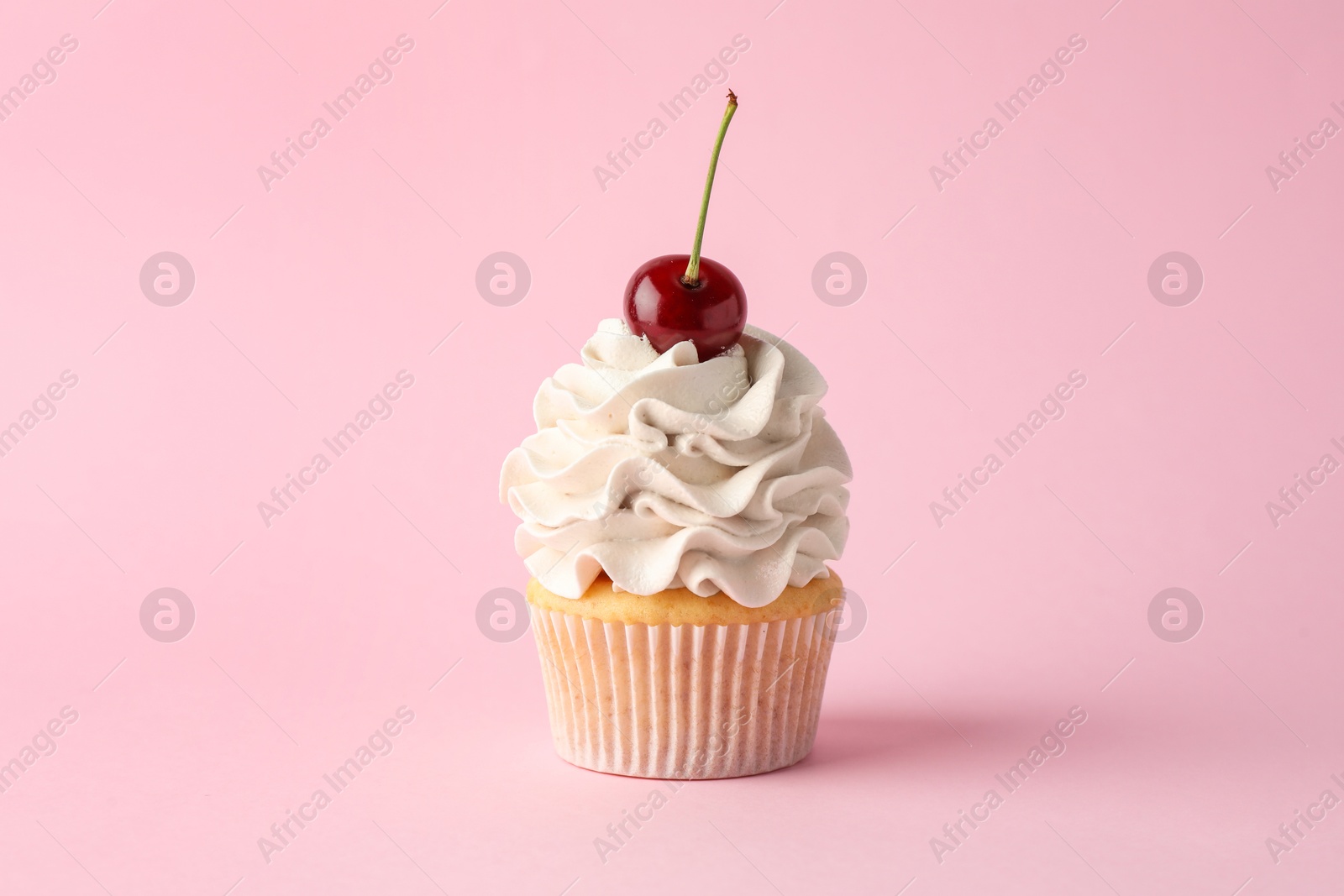 Photo of Delicious cupcake with cream and cherry on pink background