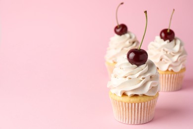 Photo of Delicious cupcakes with cream and cherries on pink background, space for text