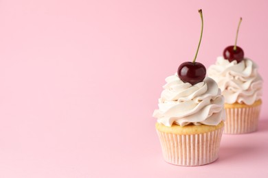 Photo of Delicious cupcakes with cream and cherries on pink background, space for text