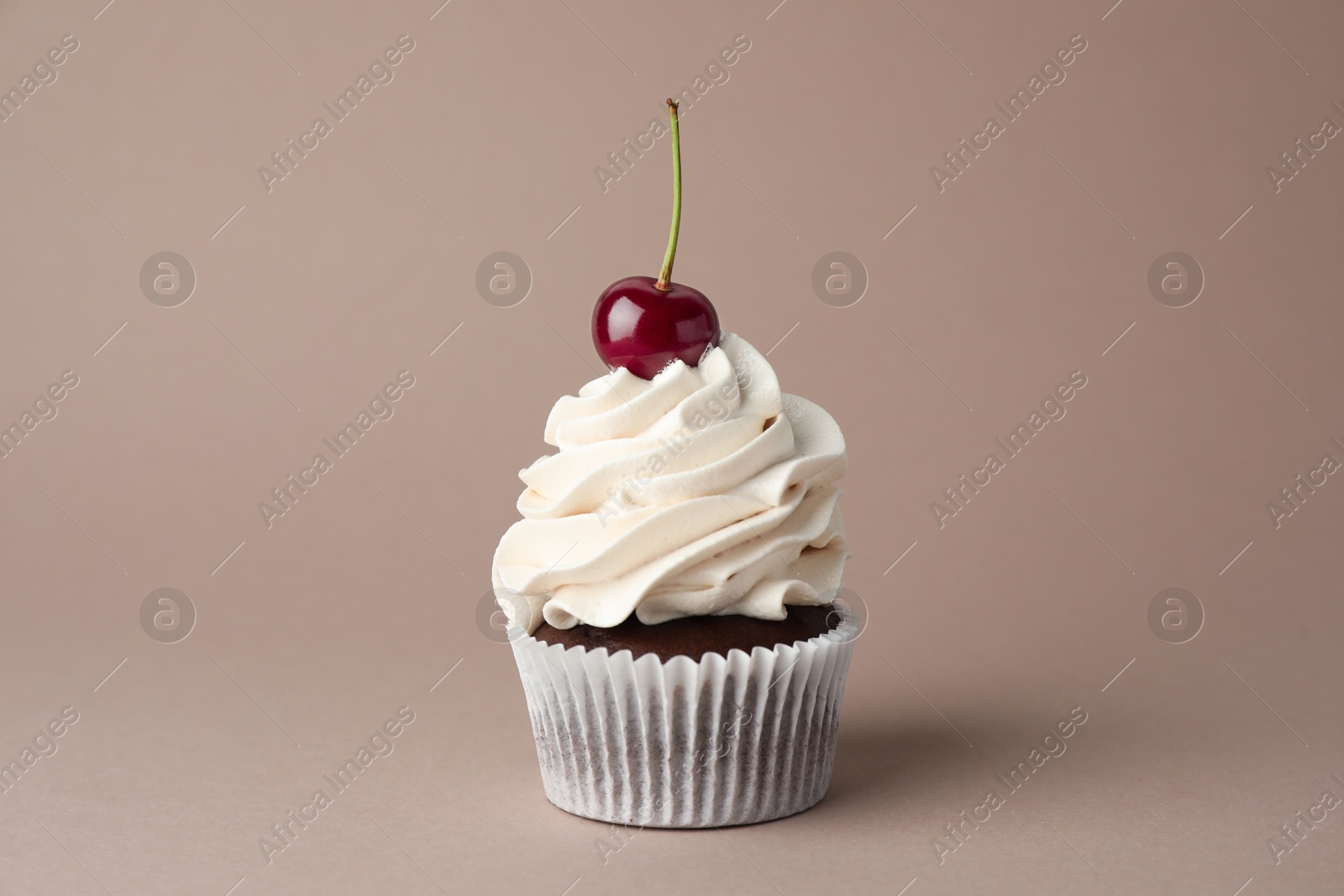 Photo of Delicious cupcake with cream and cherry on dark beige background