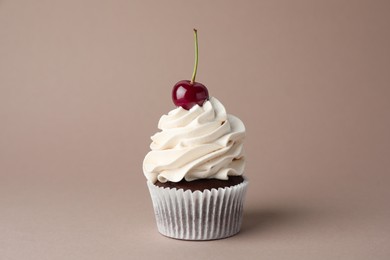 Photo of Delicious cupcake with cream and cherry on dark beige background