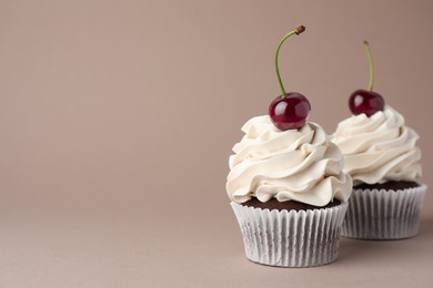 Photo of Delicious cupcakes with cream and cherries on dark beige background, space for text