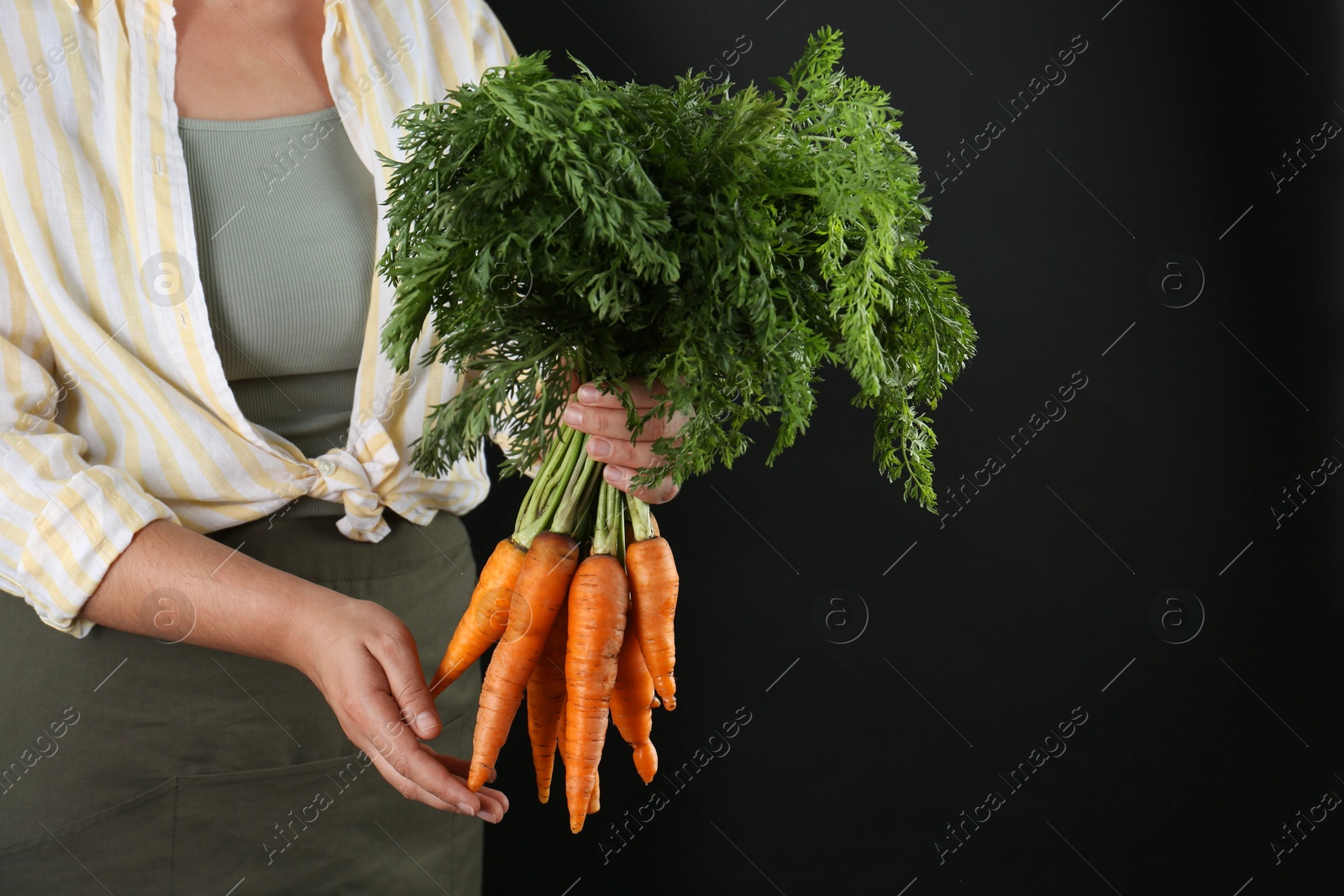 Photo of Woman holding ripe carrots on black background, closeup. Space for text