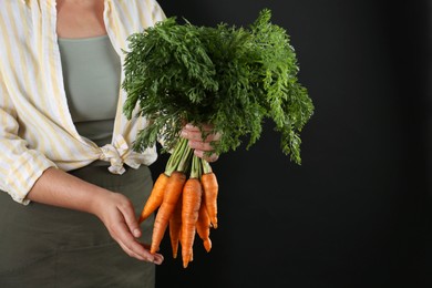 Photo of Woman holding ripe carrots on black background, closeup. Space for text