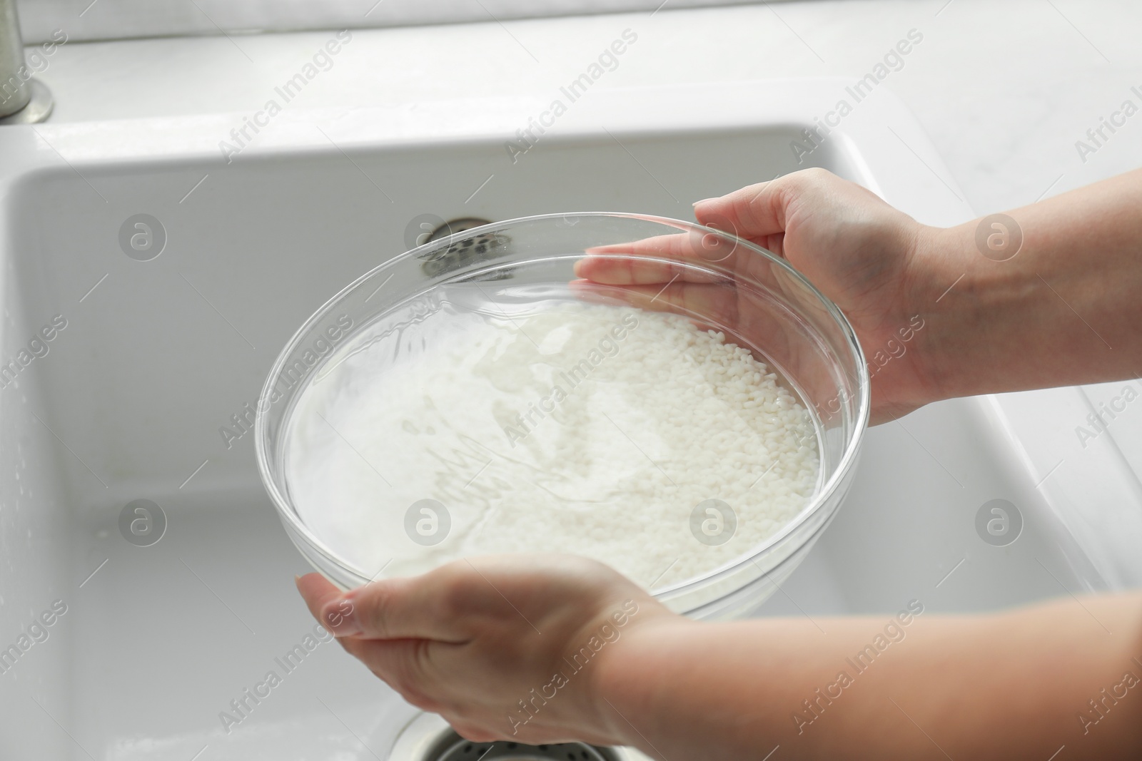 Photo of Woman holding bowl with rice and water above sink, closeup