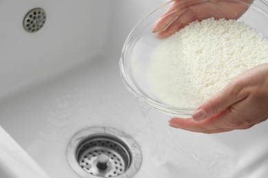 Photo of Woman rinsing rice in bowl above sink, closeup