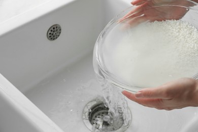 Photo of Woman rinsing rice in bowl above sink, closeup