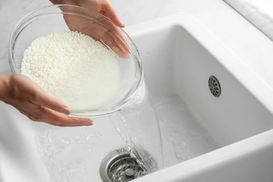 Photo of Woman rinsing rice in bowl above sink, closeup