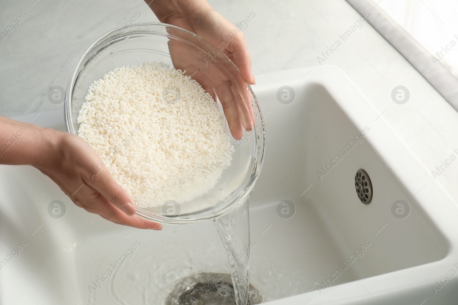 Photo of Woman rinsing rice in bowl above sink, closeup