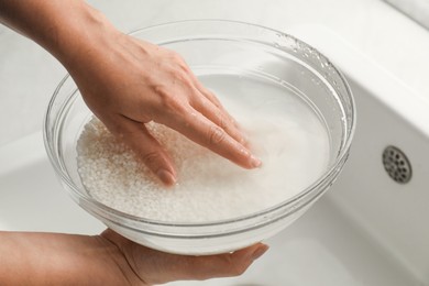 Photo of Woman rinsing rice in bowl above sink, closeup