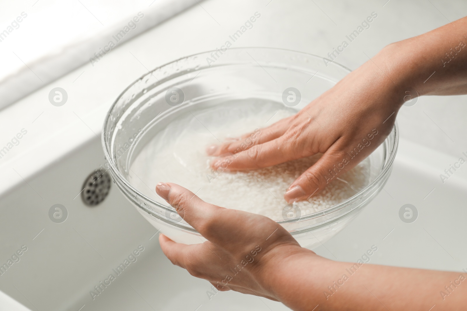 Photo of Woman rinsing rice in bowl above sink, closeup