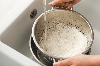 Photo of Woman rinsing rice in colander at sink, closeup