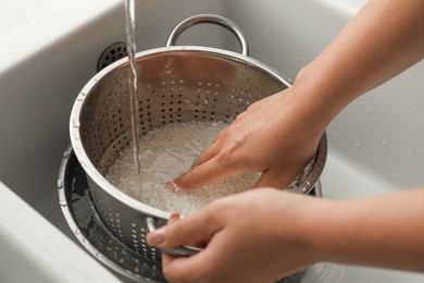 Woman rinsing rice in colander at sink, closeup