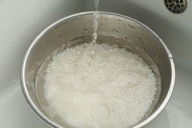 Photo of Pouring water into bowl with rice in sink, closeup