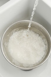 Pouring water into bowl with rice in sink, closeup