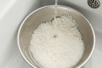 Photo of Pouring water into bowl with rice in sink, closeup