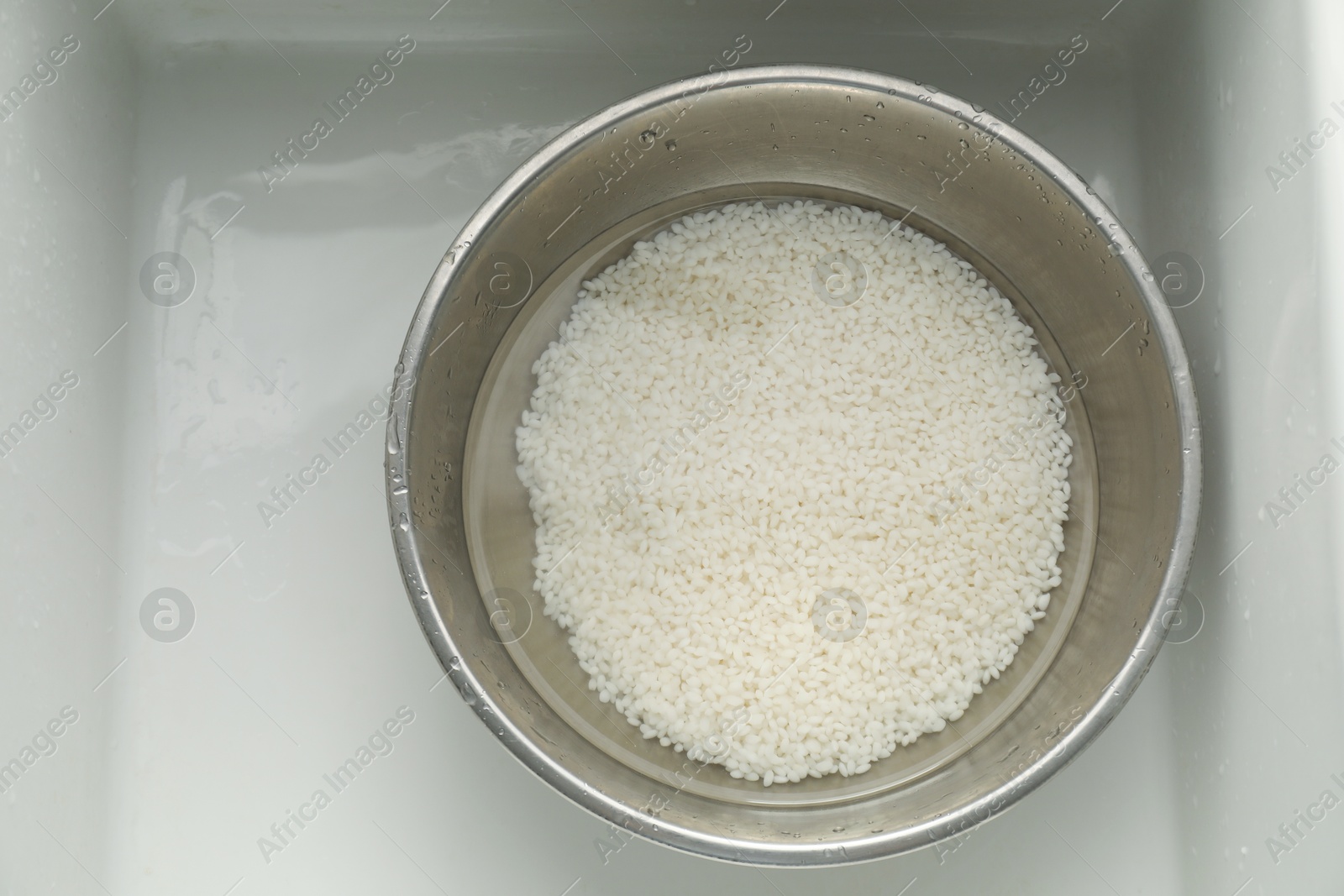 Photo of Raw rice in bowl with water in sink, top view