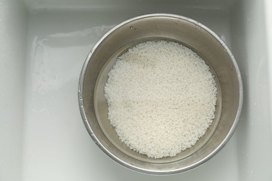 Photo of Raw rice in bowl with water in sink, top view