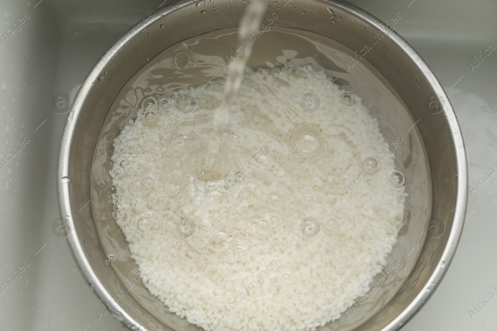 Photo of Pouring water into bowl with rice in sink, top view