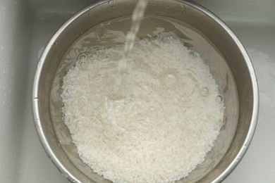 Pouring water into bowl with rice in sink, top view