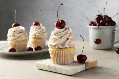 Delicious cupcakes with cream and cherries on light textured table