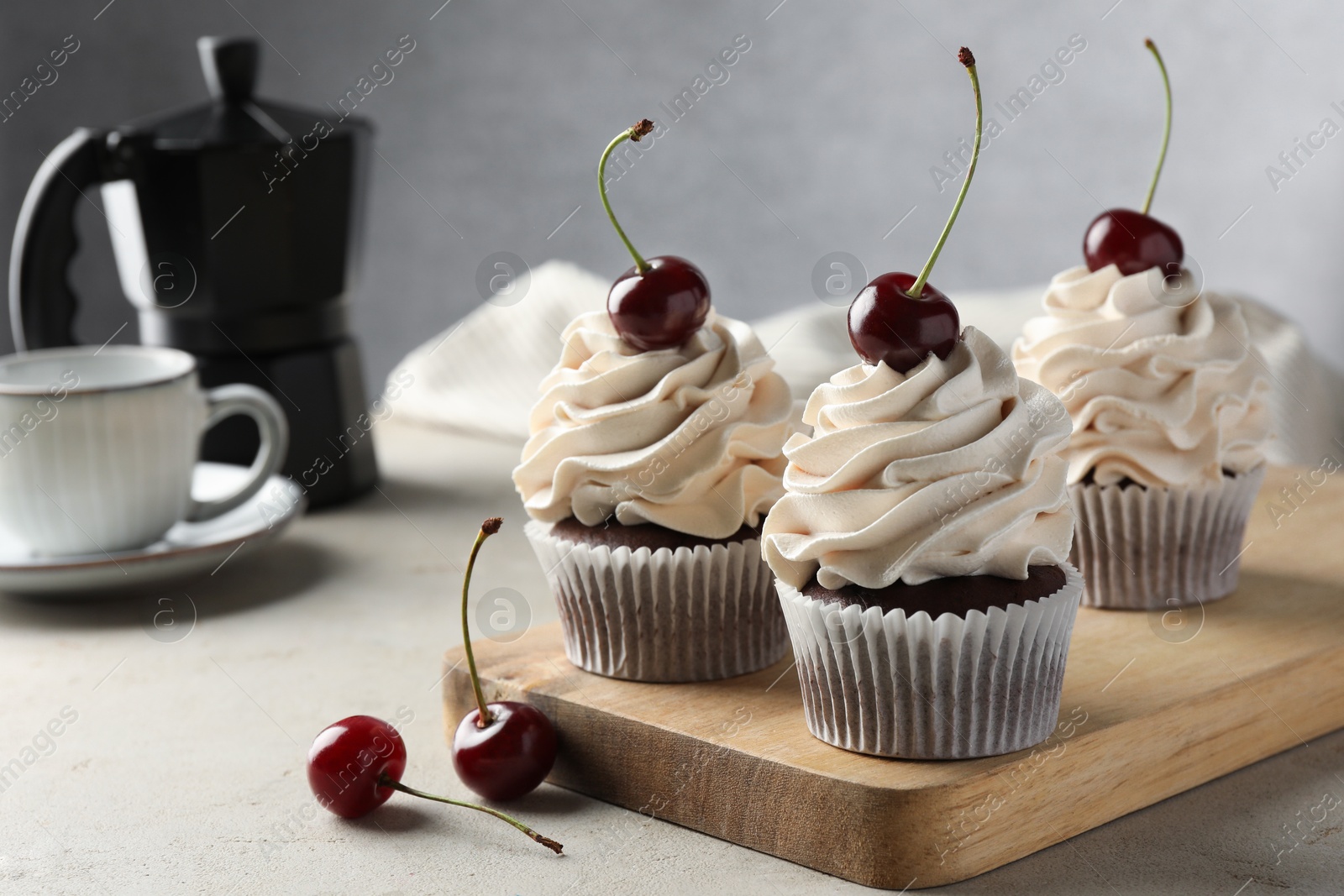 Photo of Delicious cupcakes with cream and cherries on light textured table